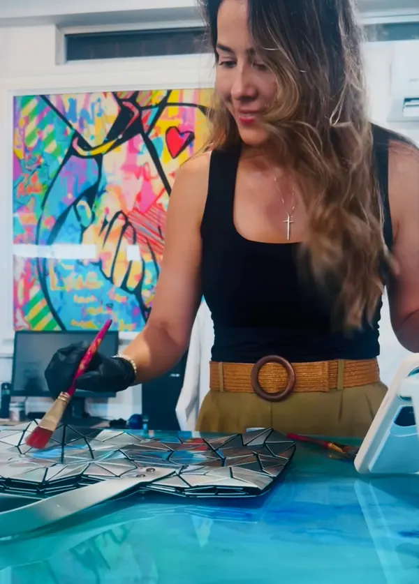 Imelda hand-painting a colorful ceramic artwork in her studio
