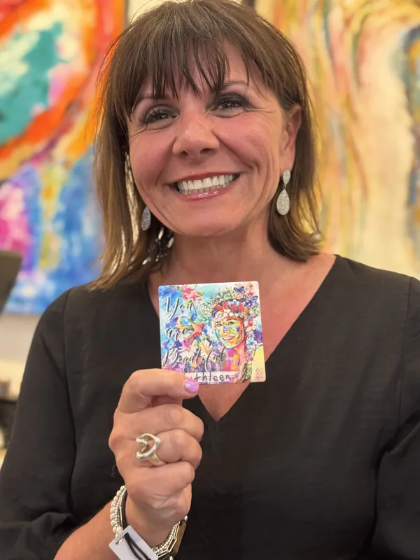 A client shows her MIA ceramic art personalized with the name Kathleen, gallery paintings glowing behind her