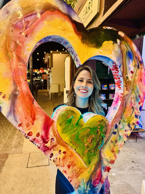 A client smiles through the giant painted heart sculpture outside the gallery in the Art District at dusk